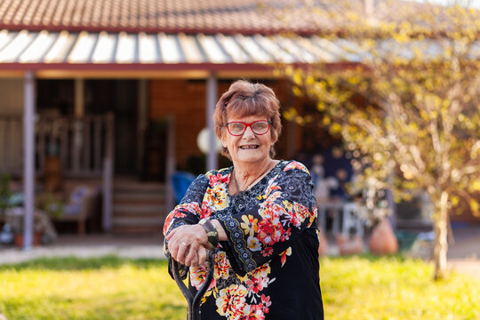 Portrait of senior woman leaning on shovel in backyard of her home