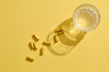 A glass of water, accompanied by yellow capsules, placed on a yellow background. Empty space for product advertising display.