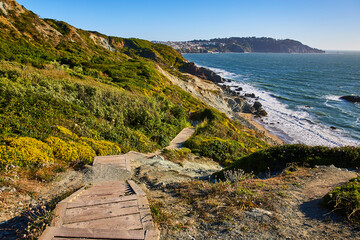Stairs with no railing going down green hill toward rocky shore with small beach and waves