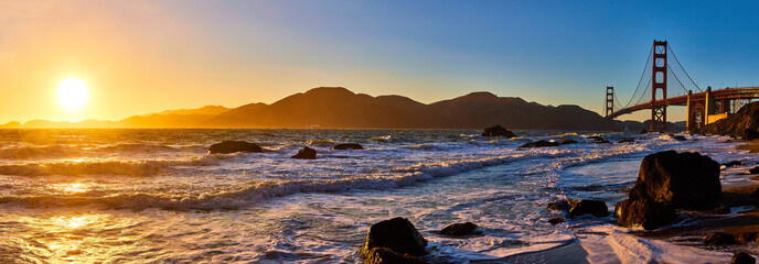 Panorama sunset over waves and distant mountain with Golden Gate Bridge
