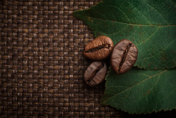 roasted coffee beans and green leaves close-up on the background of a bag
