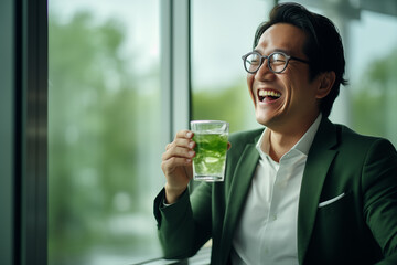 Asian male employee holding green healthy fruit and vegetable juice in the office - obrazy, fototapety, plakaty