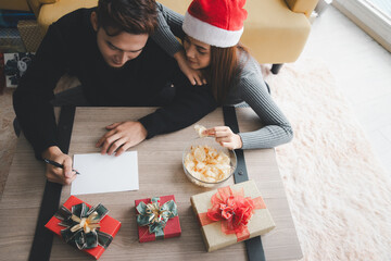 Top view of young lover couple is writing to do list and goals in a blank paper sheet for New year, Christmas on wooden table background