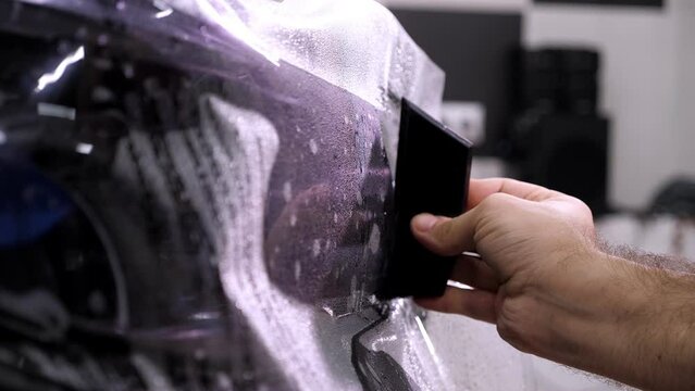 Car wrapping specialist putting vinyl foil or film. Protective film on the vehicle. Applying a protective film to the car with tools for work. Car detailing. Transparent film. Car paint protection.