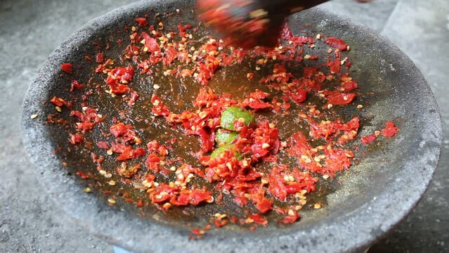 An asian hand pounding red chili and lime with stone mortar and pestle. Process to make sambal, an Indonesian condiment food