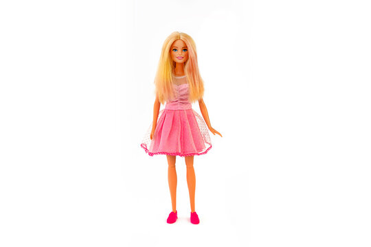 Barbie doll with loose blond hair in a pink dress standing isolated on a white background.
