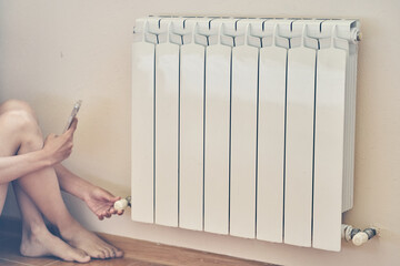 The woman turns down the heating on the radiator. Economic crisis and despair in cold houses....