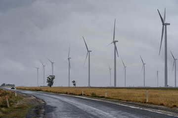 Low angled view of a rural road and cluster of wind turbines against a dark stormy sky near Dimboola