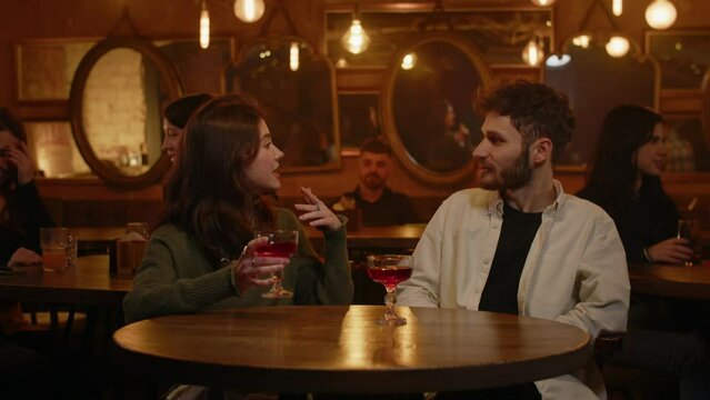 Two strangers mets at bar and flirting when drinks alcohol. Cheers, let's drink for this beautiful summer evening. Happy couple sitting on free place in night pub. A date inside cafeteria