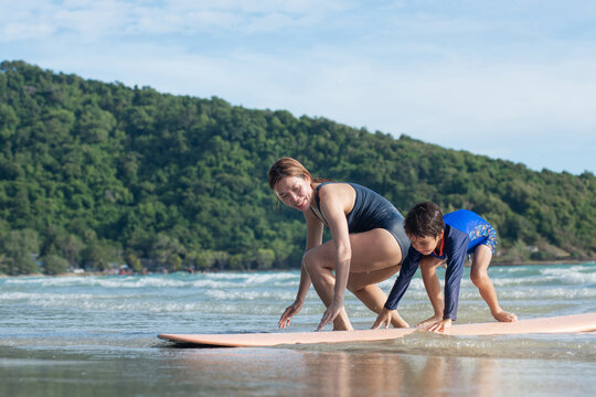 Mother teaches son the basics of surfing, surfing lessons on the beach, lifestyle activities, water sports