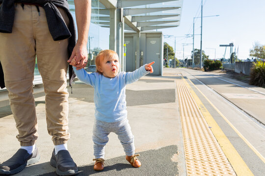 Young toddler pointing at tram station platform holding parents hand