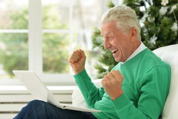 Fototapeta premium Excited middle aged senior man euphoric winner. Older mature grandfather looking at laptop reading great news getting good result winning online bid feeling amazed. Winning gesture