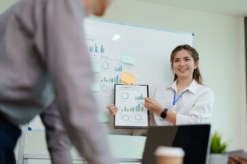 Fototapeta premium portrait of young asian business team presents business profits to colleagues at meeting, explaining business turn over on flipchart to coworkers in office with using tablet.