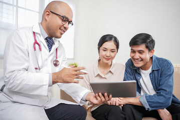 Male doctor giving test result to asian couple patient with tablet. They feeling happy and holding hand together when received good news from the doctor in medical office, hospital, clinic or home.