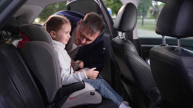 Smiling little girl gets into child seat under loving father control in car