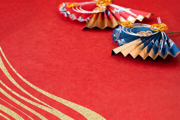 日本の正月　水引飾りのついた赤い扇と紺の扇と金色の波型の合成（赤い和紙の背景）	
