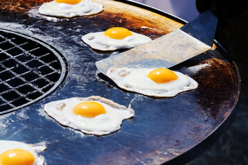 Fried eggs on a large grill. The process of preparing breakfast on fire and coals. Close-up. Selective focus
