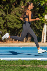 Beautiful young slim tanned runner girl, concentrated, dressed in tight sportswear, in the air running on a blue track, with style and perfect position.