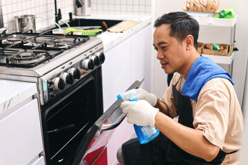 Male cleaning kitchen stove with detergent spray bottle and cloth