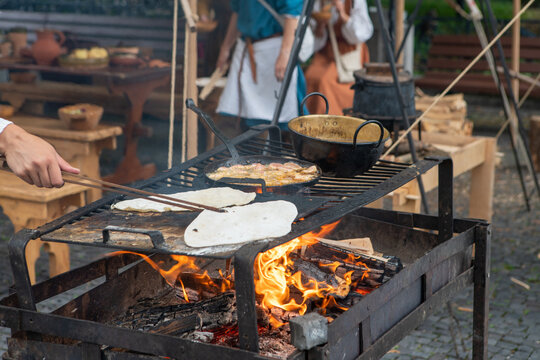Woman preparing a natural flatbread on the open fire on the metal leaf during traditional annual medieval ages restoration. Healthy food and nutrition concept image.