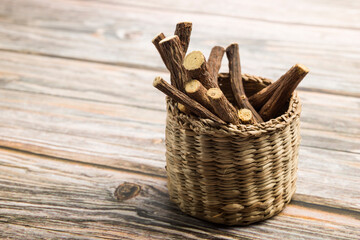 Sticks of liquorice roots on little basket on wooden table.