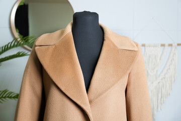 Double-breasted coat in double camel fabric with a wide collar. Demonstration of clothing on a tailor's mannequin. Detail of demi-season outerwear.