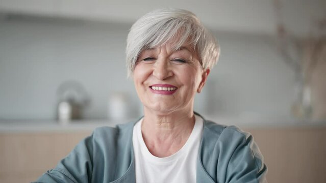 Portrait smiling mature woman. Older lady looking camera and shows white teeth. Old lady posing home. Positive single senior retired female. Gray-haired woman enjoying life, good mood. Retirement age.