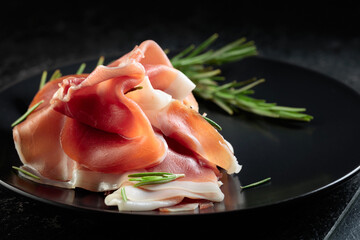 Prosciutto with rosemary on a black plate.