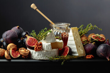 Camembert cheese with fruits and honey on a black background.