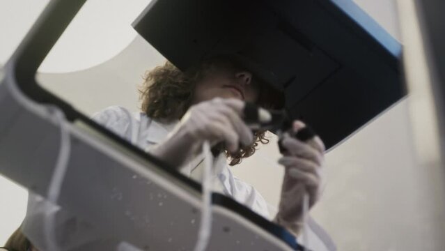 A medic girl controls a medical robot Da Vinci. A woman doctor performs an innovative remote operation. A female holds a surgical scalpel control tool in her hands. Cancer treatment in virtual reality