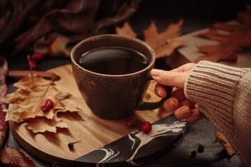 Morning cup of coffee with dried leaves. Woman's hand holding cup. Cozy autumn composition with hot...
