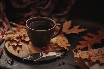 Cozy scene for cold weather with cup of coffee and dried leaves. Autumn composition with hot beverage, book and foliage. Autumnal mood, hygge lifestyle concept