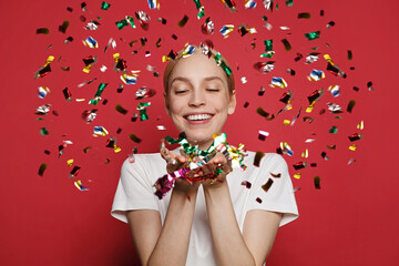 People, holidays, emotion and glamour concept. Happy young woman confetti against red studio wall...