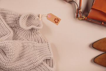 Autumn design second hand idea, zero waste, eco friendly concept. Knitted sweater made from recycled material with recycling symbol tag, shoes and bag on beige background