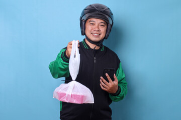 Smiling online motorcycle taxi driver holding food wrapped in plastic while holding smartphone,...
