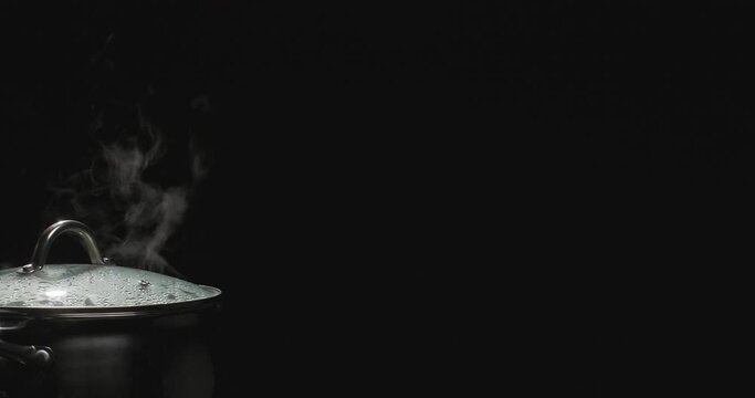 Steaming pan on a black background. Chef opening the lid of the pan with boiling water. Steam comes out of the saucepan while cooking. Boiling water in a pan on black background. Slow motion