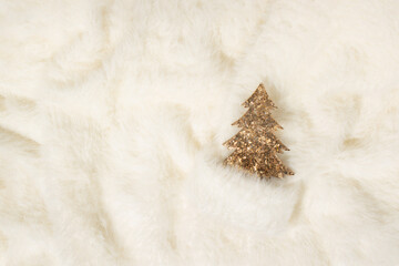 Shiny golden Christmas tree decoration on white fur background. Winter cozy holiday concept.