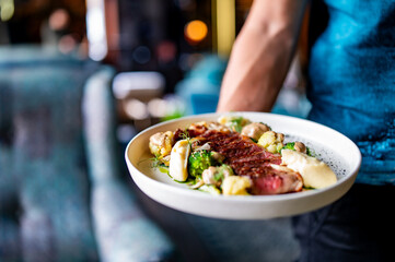 waiter hold sliced beef steak rare with green broccoli and potato