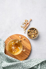 Chamomile herbal tea in a glass cup on a wooden board on a light background with dry flowers. The concept of a healthy detox drink for health and sleep.