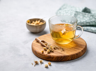 Chamomile herbal tea in a glass cup on a wooden board on a light background with dry flowers. The concept of a healthy detox drink for health and sleep