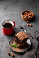 A stack of chocolate brownies with mint and  hazelnuts on a dark  background with cup of coffee and nuts. The concept of delicious and sweet homemade baked goods.