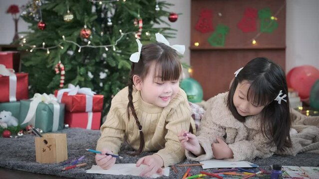Shot in slow motion of cute little girls lying on floor in living room and making Christmas greeting card
