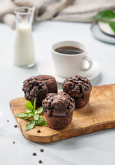 Chocolate muffins on a wooden board with mint on a light background with cup of coffee and milk. The concept of healthy homemade baked