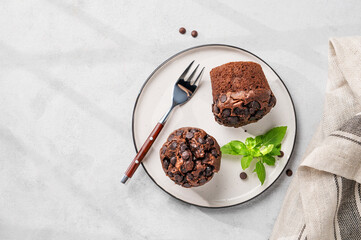 Chocolate muffins on a white plate with mint on a light background. Healthy homemade baking concept.