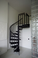 Black metal spiral staircase in a bright room. Glass tiles, minimalist style