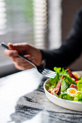 Hands of a man with a fork eat Salad nicoise. Tuna, with green beans, tomatoes, potatoes and a vinaigrette mustard dressing in white plate