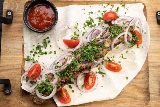Juicy hot lula kebab made from meat and spices. Serving dishes in a restaurant on pita, over wooden board, top view. Georgian cuisine