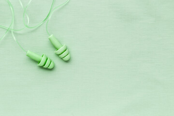 Reusable silicone earplugs green color on colored cloth background, copy space. Soft, flexible ear plug on cord, for swim, sleep, against noise, protect hear, monochrome top view, minimal trend