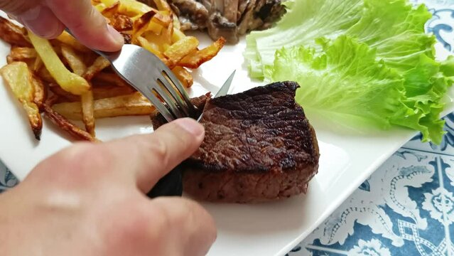 gros plan sur les mains d'une personne coupant un morceaux de boeuf grill&eacute; dans une assiette