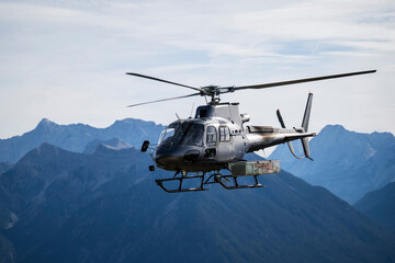Dark gray cargo helicopter with accessories basket on the side flies in the mountains of the...